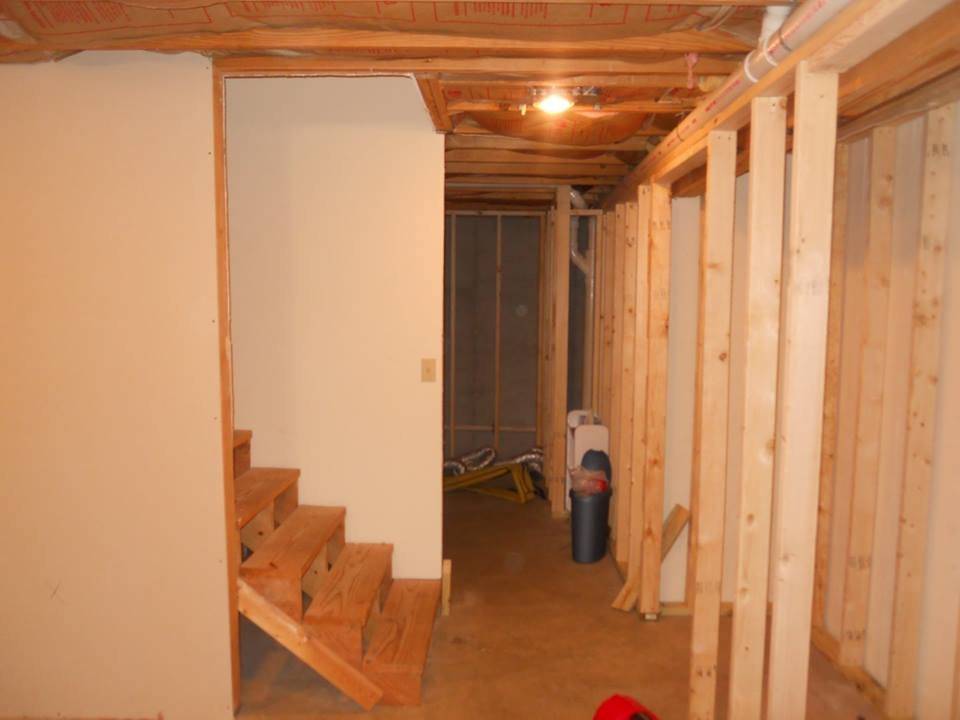 A basement mid-renovation with new stud walls framed out, drywall partly hung, and a new set of wooden stairs built in